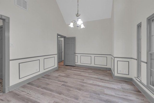 unfurnished dining area featuring an inviting chandelier, high vaulted ceiling, and light hardwood / wood-style flooring