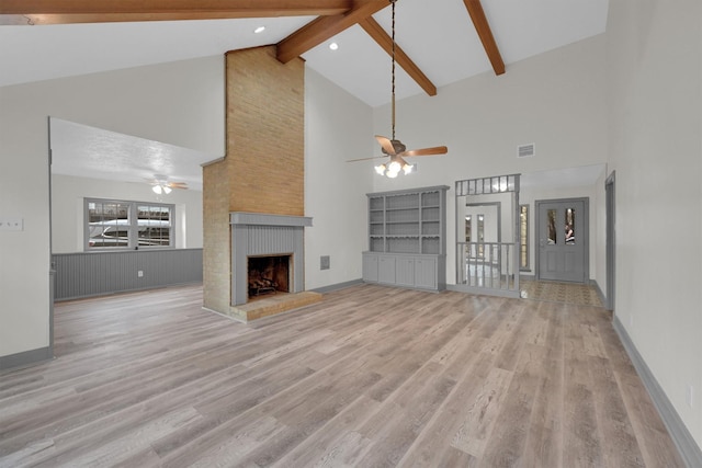 unfurnished living room featuring beam ceiling, a fireplace, ceiling fan, and light wood-type flooring