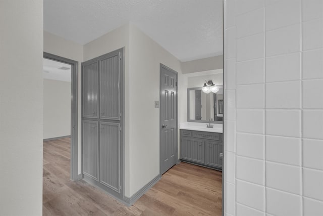 hallway with sink, a textured ceiling, and light hardwood / wood-style floors