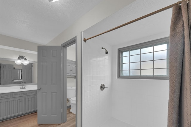 bathroom featuring toilet, a textured ceiling, a tile shower, vanity, and hardwood / wood-style flooring