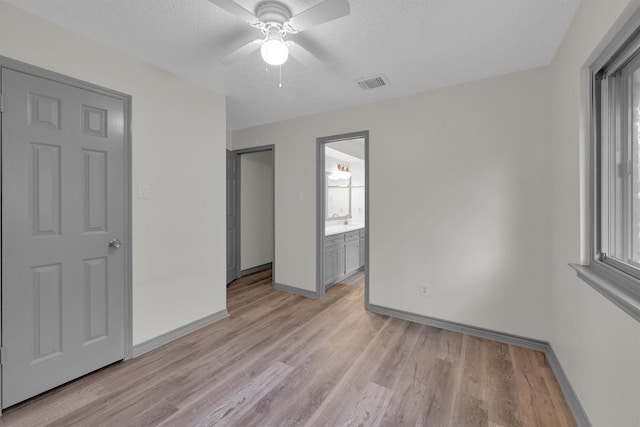 unfurnished bedroom featuring connected bathroom, sink, light hardwood / wood-style flooring, and a textured ceiling