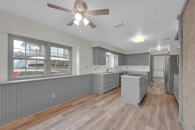 kitchen with sink, a textured ceiling, appliances with stainless steel finishes, gray cabinets, and light hardwood / wood-style floors