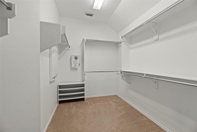 walk in closet with vaulted ceiling and light colored carpet