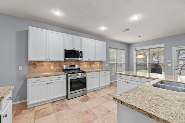 kitchen with sink, appliances with stainless steel finishes, backsplash, white cabinets, and decorative light fixtures