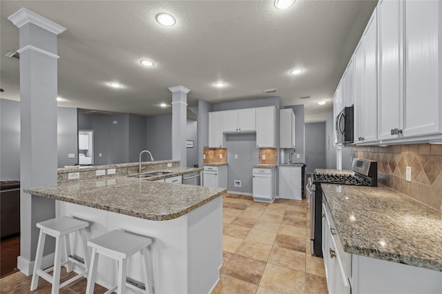 kitchen with sink, appliances with stainless steel finishes, backsplash, white cabinets, and ornate columns