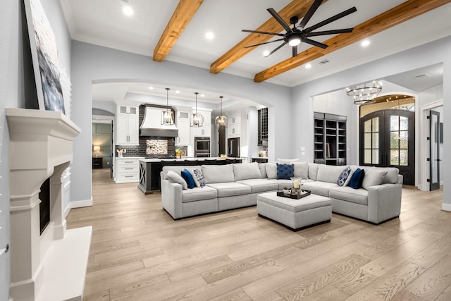 living room with beamed ceiling, ceiling fan with notable chandelier, light hardwood / wood-style floors, and french doors