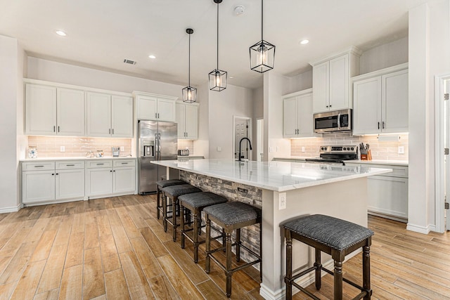 kitchen featuring a breakfast bar area, white cabinetry, decorative light fixtures, a center island with sink, and appliances with stainless steel finishes