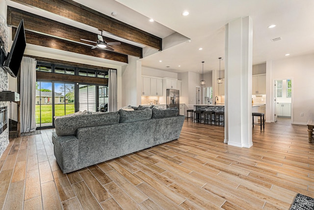 living room with beamed ceiling, ceiling fan, a fireplace, and sink