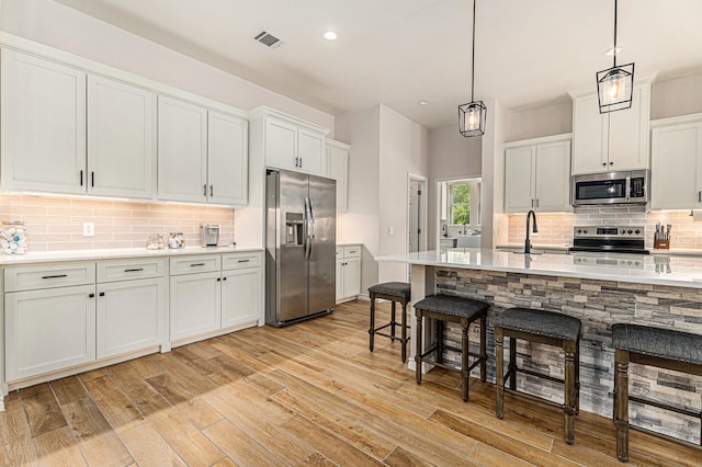 kitchen with sink, white cabinetry, hanging light fixtures, stainless steel appliances, and decorative backsplash