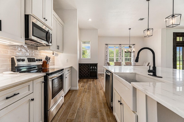 kitchen featuring appliances with stainless steel finishes, dark hardwood / wood-style floors, decorative light fixtures, white cabinets, and light stone counters