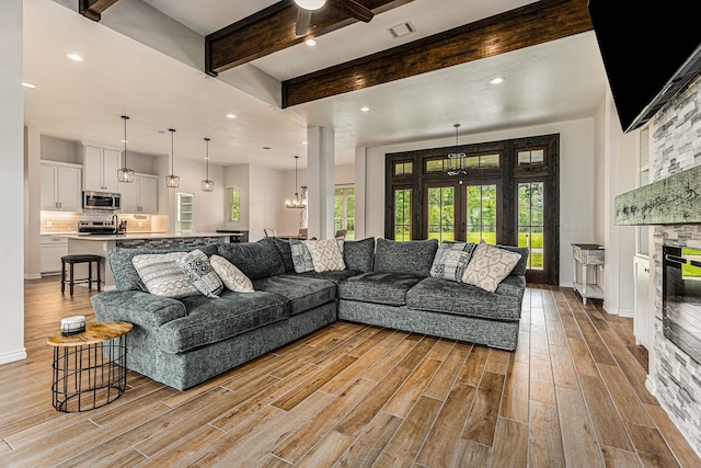 living room featuring beamed ceiling, a notable chandelier, a fireplace, and french doors