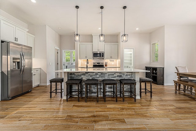 kitchen featuring white cabinetry, appliances with stainless steel finishes, hanging light fixtures, and a center island with sink