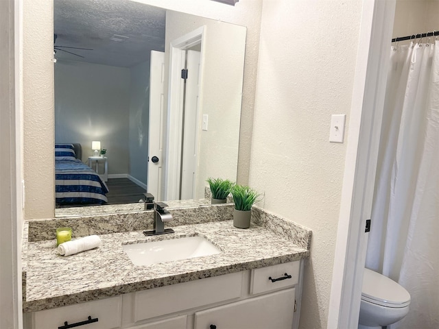 bathroom with ceiling fan, vanity, toilet, and a textured ceiling