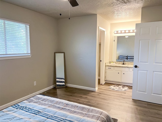 bedroom featuring ensuite bathroom, sink, ceiling fan, a textured ceiling, and light hardwood / wood-style flooring