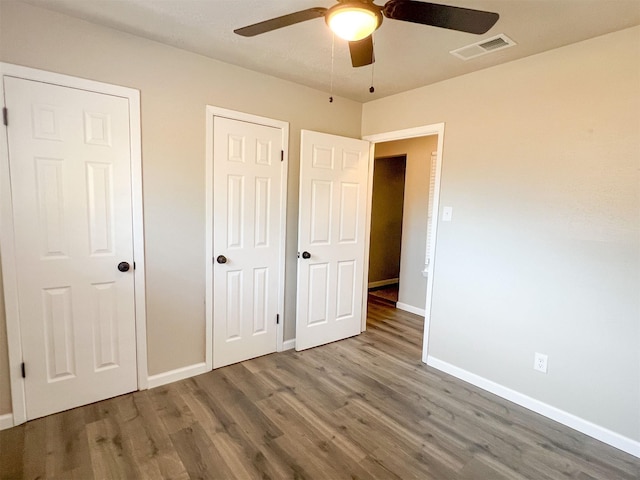 unfurnished bedroom with dark hardwood / wood-style floors, two closets, and ceiling fan