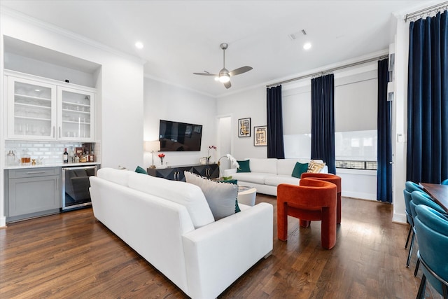 living room with dark wood-type flooring, ornamental molding, beverage cooler, and bar area