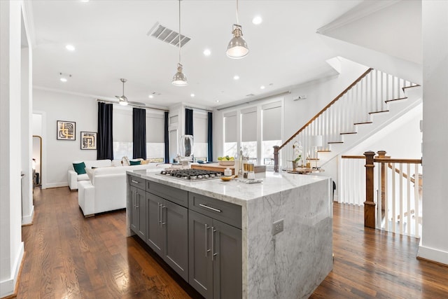 kitchen featuring gray cabinets, decorative light fixtures, ornamental molding, a center island, and light stone counters