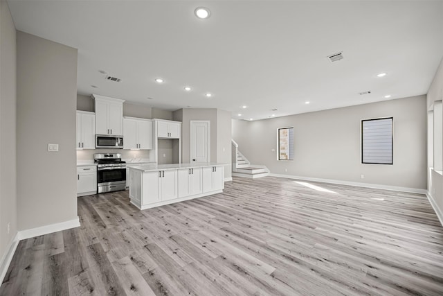 kitchen featuring stainless steel appliances, an island with sink, white cabinets, and light wood-type flooring