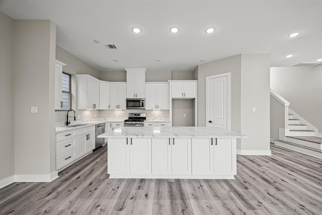 kitchen with white cabinetry, sink, a center island, light stone counters, and stainless steel appliances