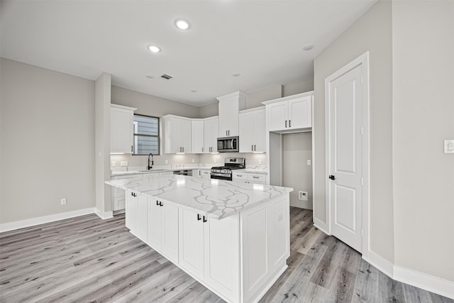 kitchen featuring sink, stainless steel appliances, a center island, light stone countertops, and white cabinets