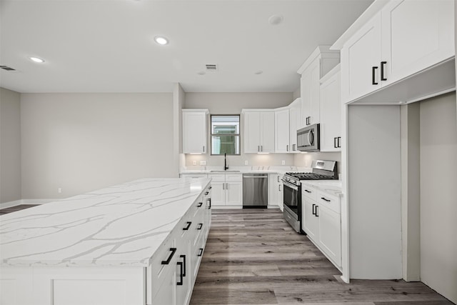 kitchen featuring sink, appliances with stainless steel finishes, a kitchen island, light stone countertops, and white cabinets