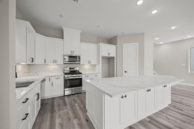 kitchen featuring light stone counters, appliances with stainless steel finishes, a center island, and white cabinets