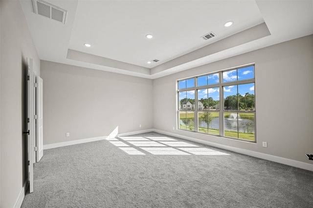 spare room featuring a tray ceiling, carpet, and a water view