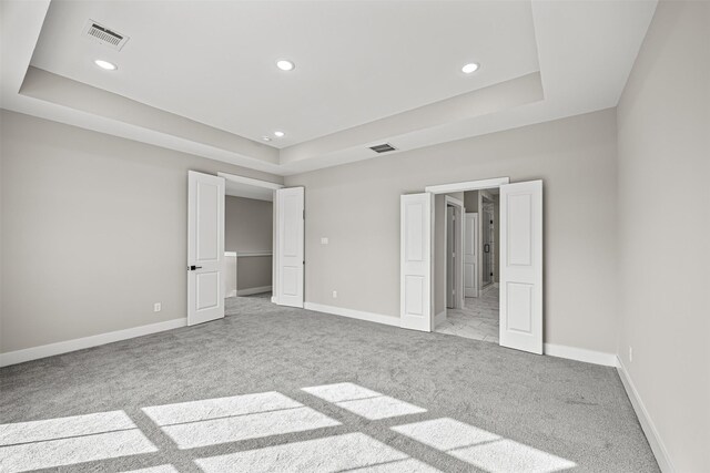 unfurnished bedroom featuring light carpet and a raised ceiling