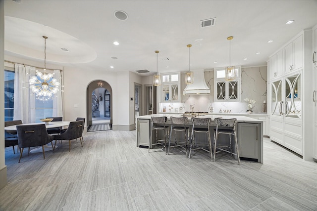 kitchen with a kitchen island, decorative light fixtures, white cabinetry, decorative backsplash, and custom range hood