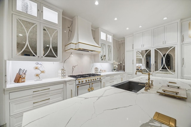 kitchen featuring premium range hood, light stone countertops, sink, and white cabinets