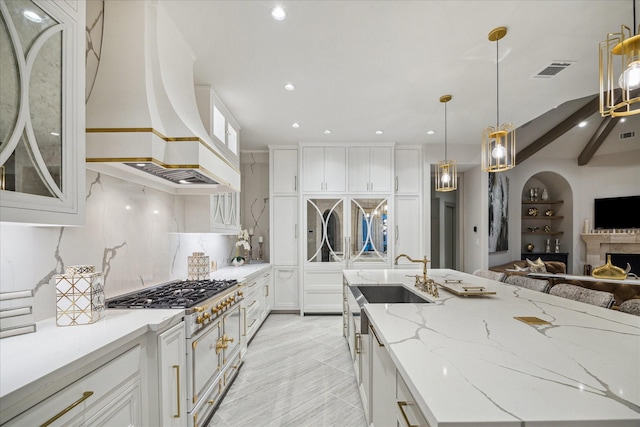 kitchen featuring sink, white cabinetry, decorative light fixtures, custom range hood, and light stone countertops