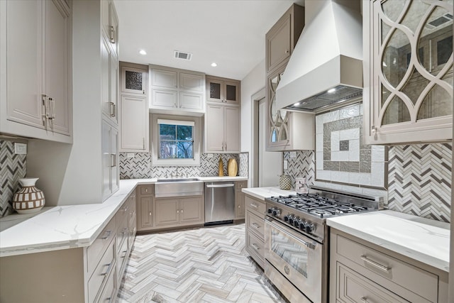 kitchen featuring light parquet floors, stainless steel appliances, light stone counters, custom range hood, and decorative backsplash