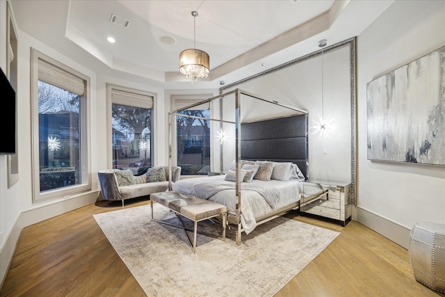 bedroom with an inviting chandelier, a raised ceiling, and hardwood / wood-style floors