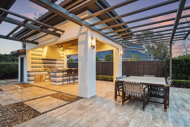 patio terrace at dusk featuring ceiling fan, area for grilling, and a pergola