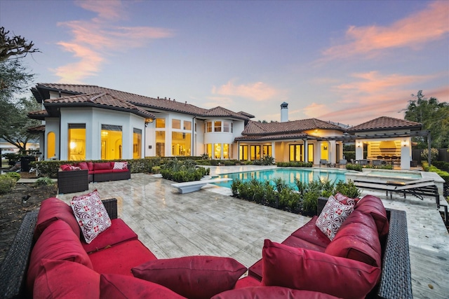 back house at dusk with a pool side deck, an outdoor hangout area, and a patio