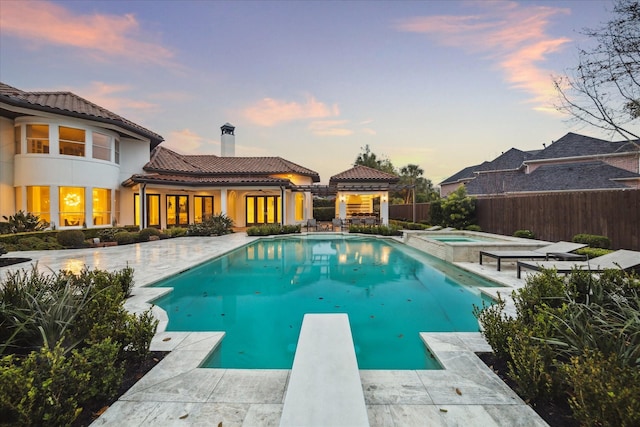 pool at dusk with a patio area, a diving board, and an in ground hot tub