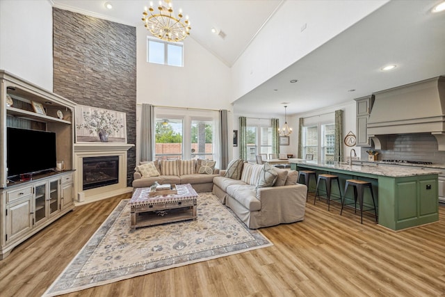 living room with sink, high vaulted ceiling, a notable chandelier, light hardwood / wood-style floors, and a large fireplace