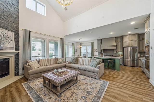 living room with crown molding, an inviting chandelier, high vaulted ceiling, a fireplace, and wood-type flooring