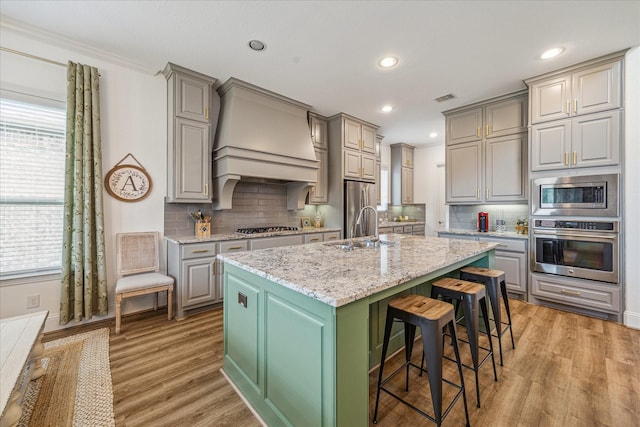 kitchen with gray cabinetry, a kitchen bar, an island with sink, and appliances with stainless steel finishes