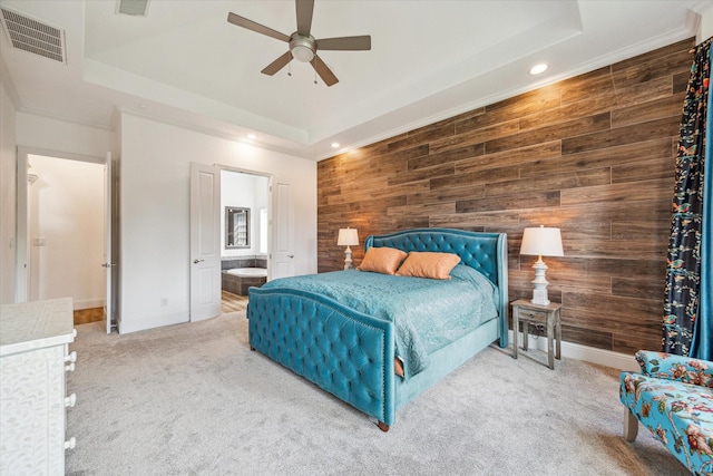 carpeted bedroom with a raised ceiling, ceiling fan, ensuite bathroom, and wooden walls