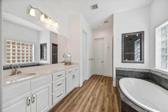 bathroom with hardwood / wood-style floors, vanity, a wealth of natural light, and a relaxing tiled tub