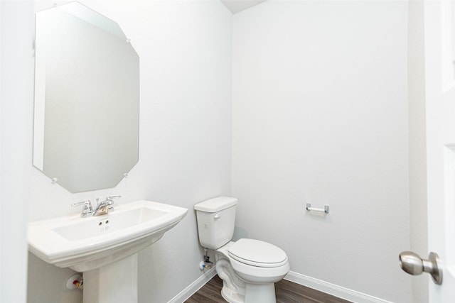 half bathroom featuring a sink, toilet, baseboards, and wood finished floors