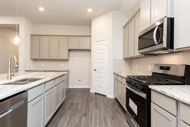 kitchen featuring light stone counters, dark wood finished floors, decorative backsplash, appliances with stainless steel finishes, and a sink