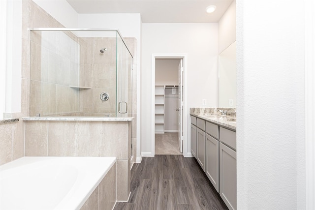 bathroom with a walk in closet, vanity, a shower stall, wood finished floors, and a bath