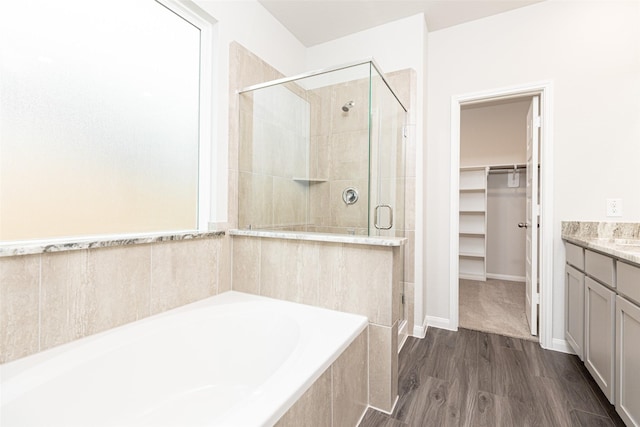 bathroom with wood finished floors, vanity, a shower stall, a bath, and a walk in closet