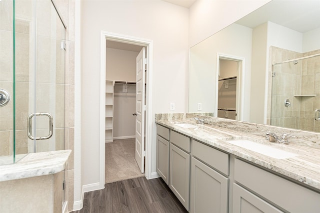 full bath featuring double vanity, a sink, a shower stall, and wood finished floors