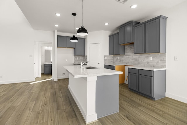 kitchen with hardwood / wood-style flooring, an island with sink, sink, and gray cabinetry