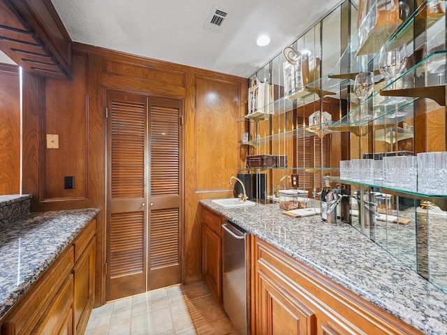 kitchen with stainless steel dishwasher, light tile patterned floors, sink, and stone counters