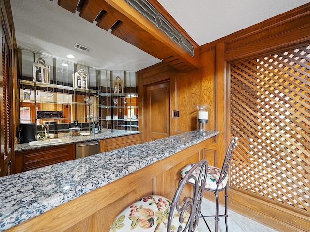 bar with stone counters, dishwasher, and sink