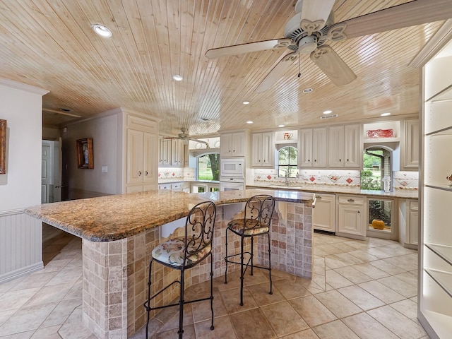 kitchen with a kitchen island, a kitchen bar, light stone countertops, wooden ceiling, and white appliances